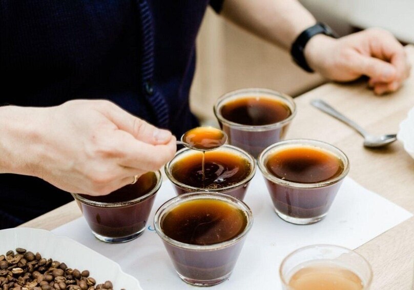A person pouring coffee into a cup, with several other cups and coffee beans visible. 5