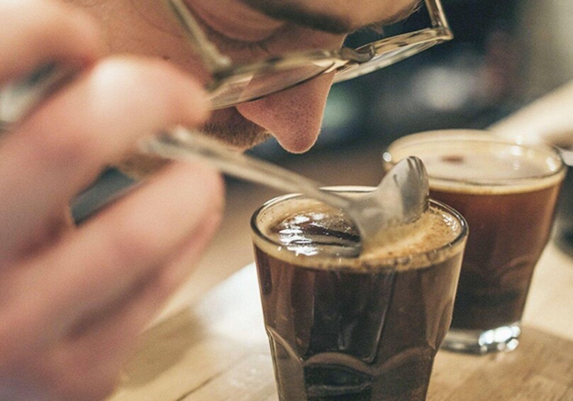 A person stirring a dark liquid in a glass with a spoon. 1