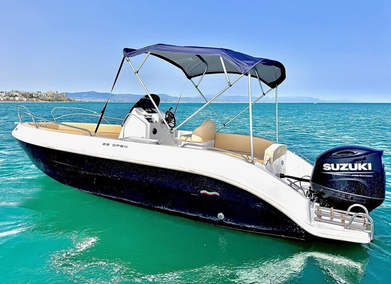 A motorboat with a Suzuki outboard motor, a canopy, and a cabin, floating on turquoise water with a coastal city in the background. 4