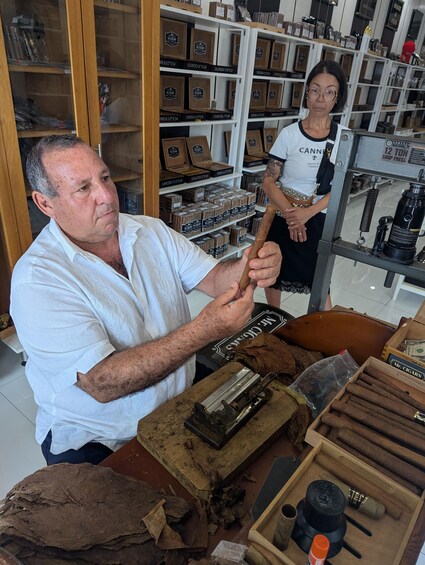 A man working with cigar components in a shop with shelves of cigar boxes. 4