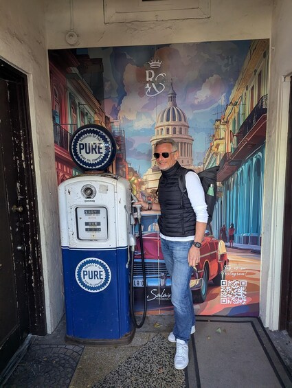 A man standing next to a vintage gas pump with a mural in the background. 5