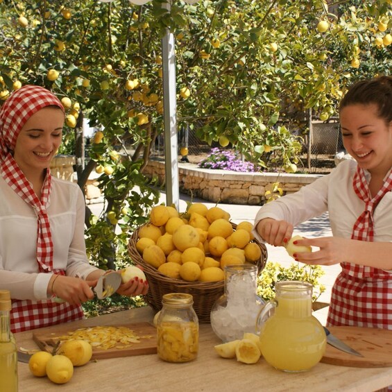 Two individuals preparing lemons outdoors, with a basket of lemons, a cutting board, and a juicer on the table. 3