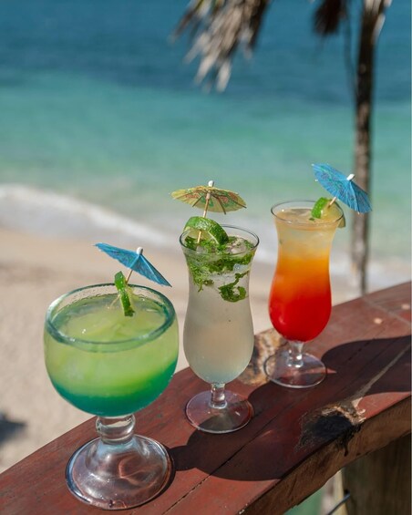 Three tropical cocktails on a wooden table with a beach and ocean in the background. 5