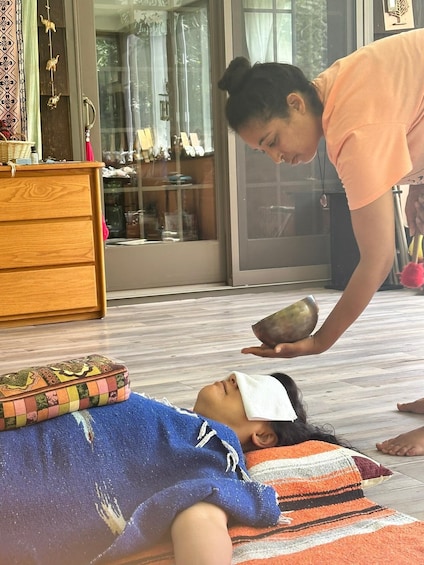 A person lying on a blue towel with a patterned blanket, receiving a head massage from another person. 3