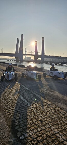 A convoy of remote-controlled cars on a cobblestone road with a bridge and river in the background. 5