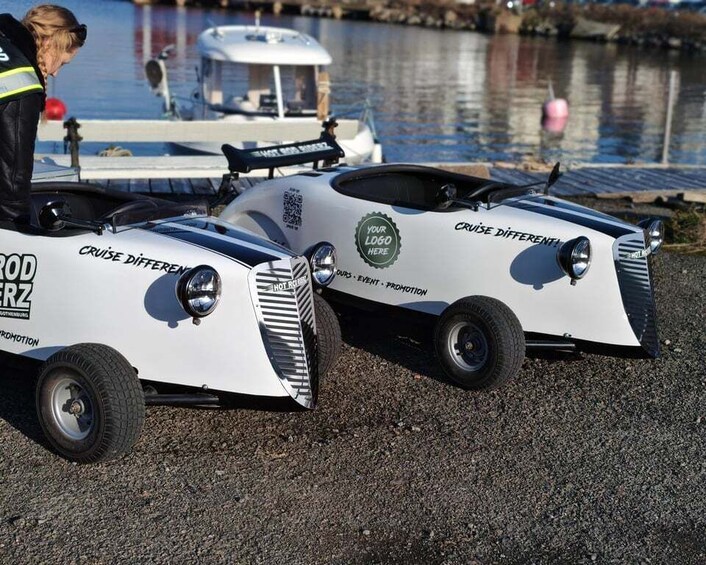Two white jet skis with 'CRUISE DIFFERENTIAL' and 'YOUR LOGO HERE' decals, parked on a gravel surface near calm water. 2