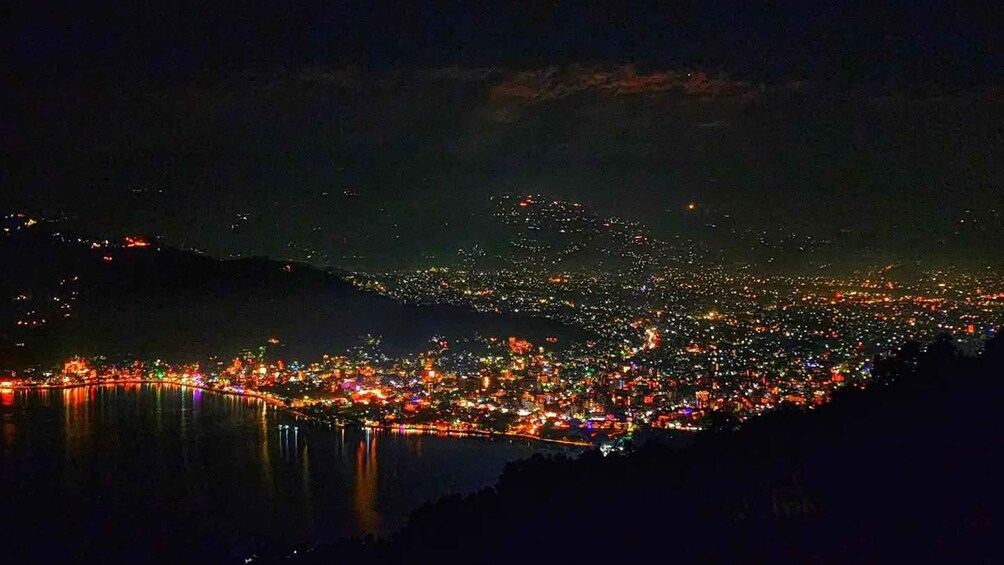 A nighttime cityscape with a river reflecting lights, a densely populated area, and distant hills. 4