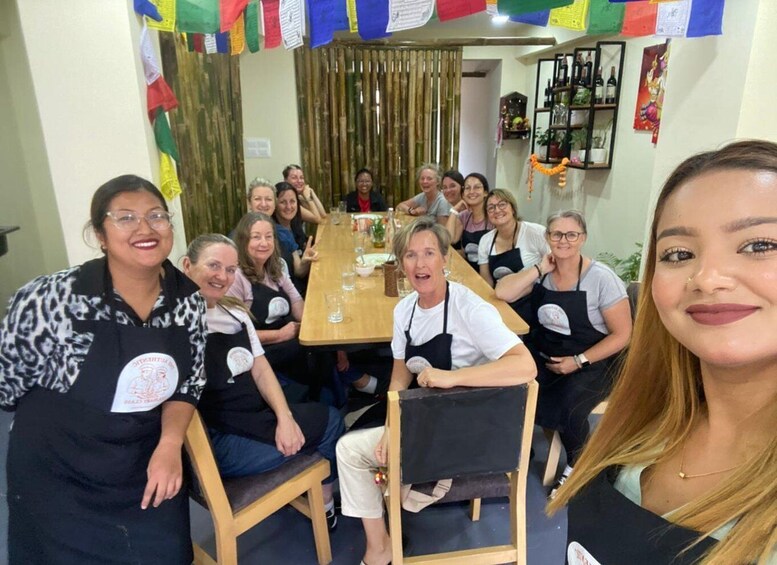 A group of people seated around a table with a bamboo curtain backdrop, wearing aprons with logos. 3
