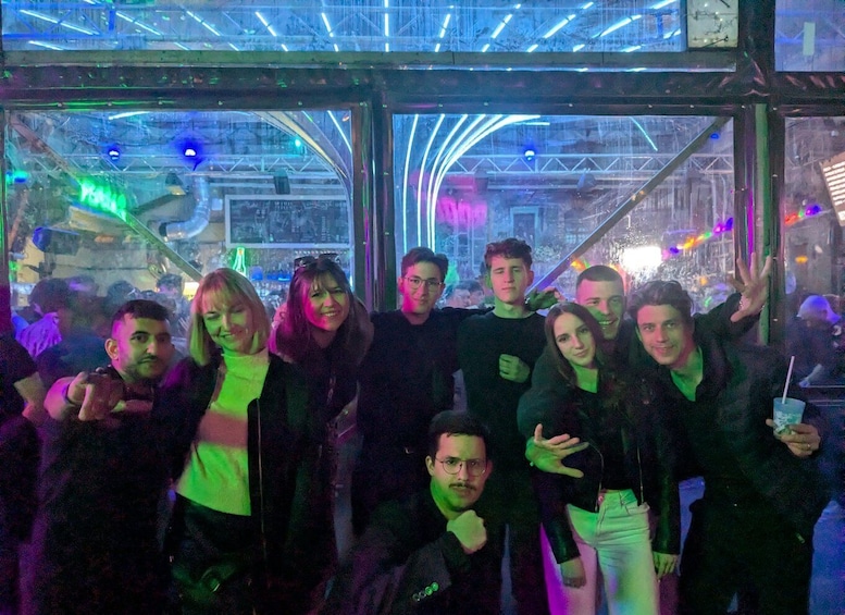 A group of people inside a glass-enclosed structure with neon lights and a cityscape view. 2