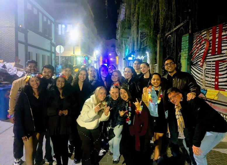 A group of people posing on a city street at night with illuminated buildings and graffiti in the background. 3
