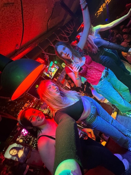 A group of people in a dimly lit indoor setting, possibly a bar or club, with colorful lighting and a festive atmosphere. 1