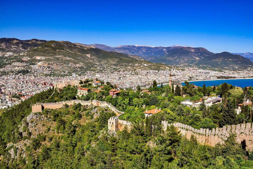 A coastal city with a historic fortress, dense urban area, and a mountain range in the background. 3