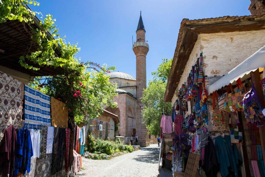 A narrow street with hanging textiles and a mosque with a minaret in the background. 1