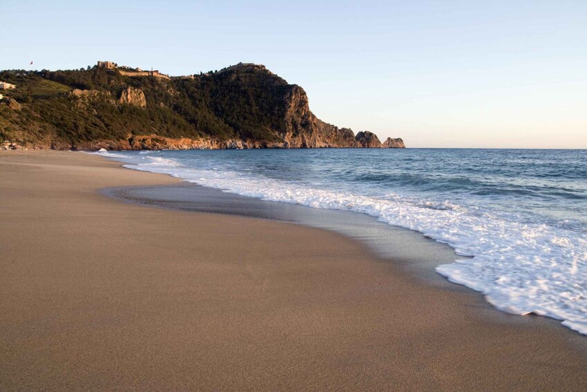 A sandy beach with gentle waves, a rocky cliff, and a castle on top. 5