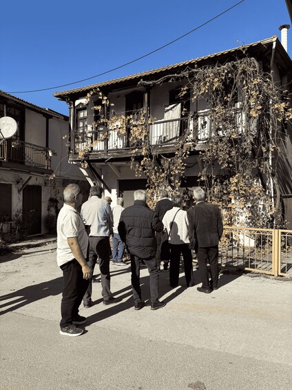 A group of people walking on a street with buildings that have balconies and vines. 2