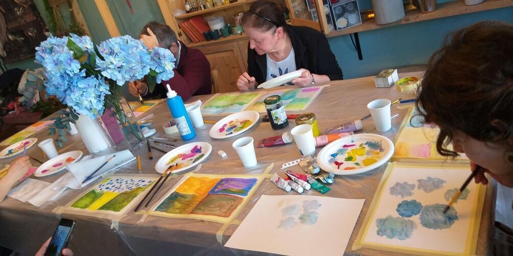 A group of people painting at a table with art supplies and canvases. 5