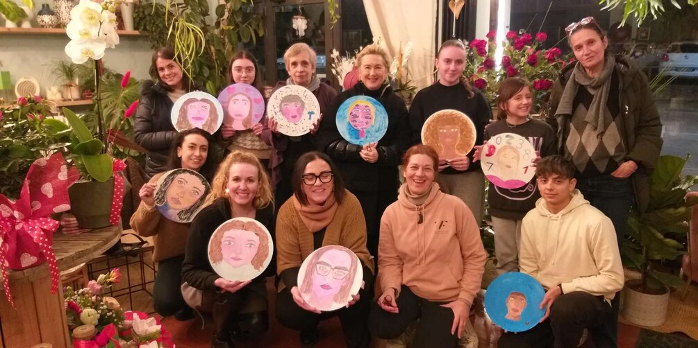 A group of people holding circular artworks with faces, surrounded by potted plants and flowers. 2