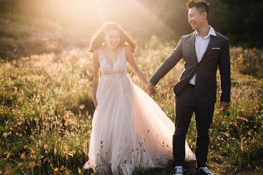 A couple holding hands in a field with tall grass and a sunset in the background. 3