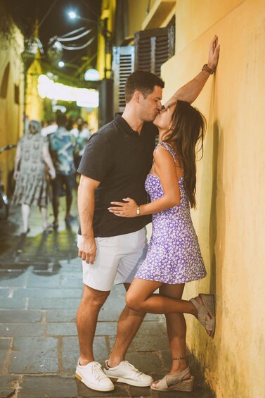 A couple embracing in a narrow street with yellow walls and overhead lights. 2