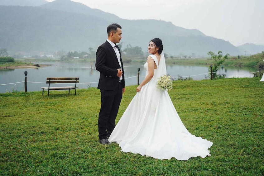 A couple in wedding attire standing on grass with a lake and mountains in the background. 4