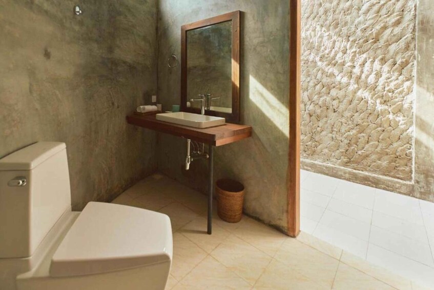 A bathroom with a white toilet, a wooden vanity with a mirror, and a textured wall. 4
