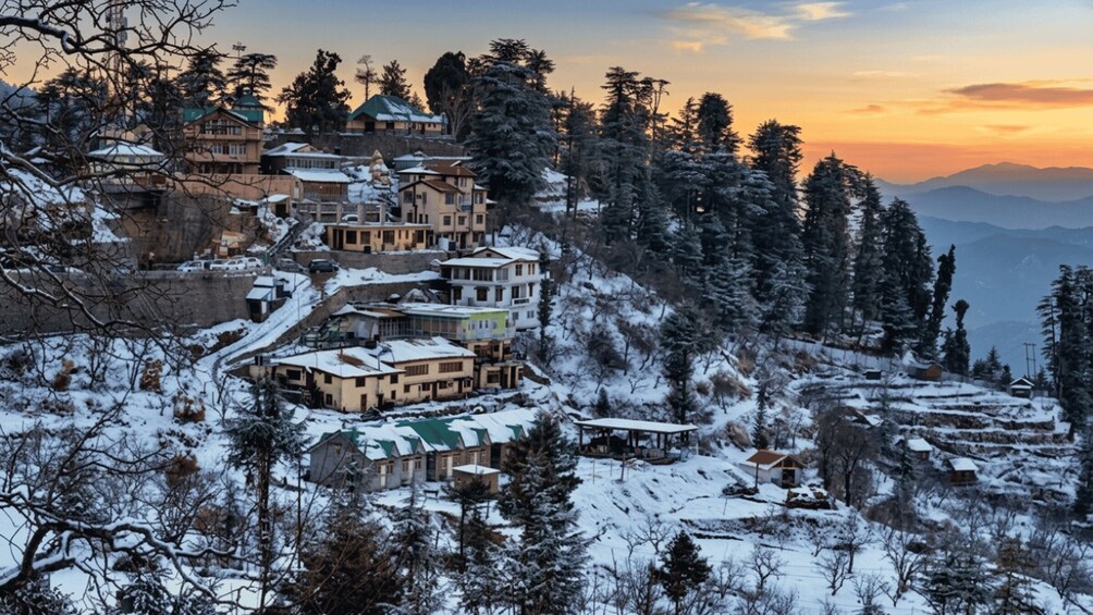 A snow-covered village with buildings on a hillside, surrounded by trees and mountains. 4