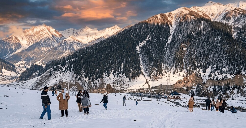 A group of people walking on a snow-covered mountain path with a backdrop of snow-capped mountains and a clear sky. 2