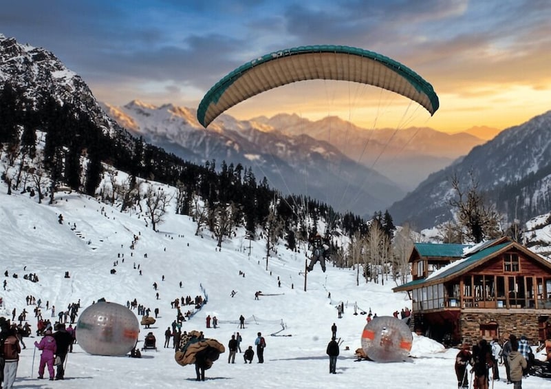 A person paragliding over a snowy mountain slope with a lodge in the background. 3