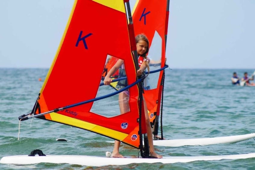 A person on a paddleboard with a red and yellow sail. 4