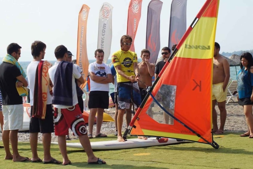 A group of people on a beach with a sailboat and flags. 2