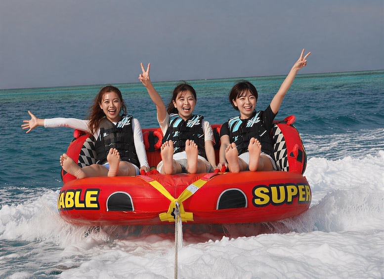 Three people on a red inflatable tube with 'TABLE' and 'SUPER' written on it, floating on water. 1