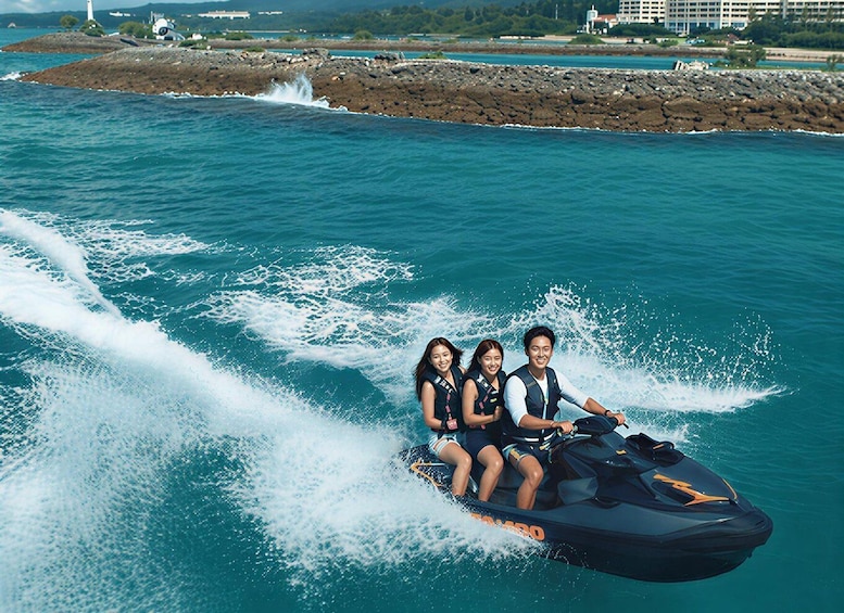 A jet ski with three people riding it, water splashing around, and a rocky shoreline in the background. 4