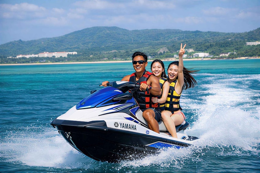 Two people on a Yamaha jet ski in turquoise waters with a mountainous coastline in the background. 2