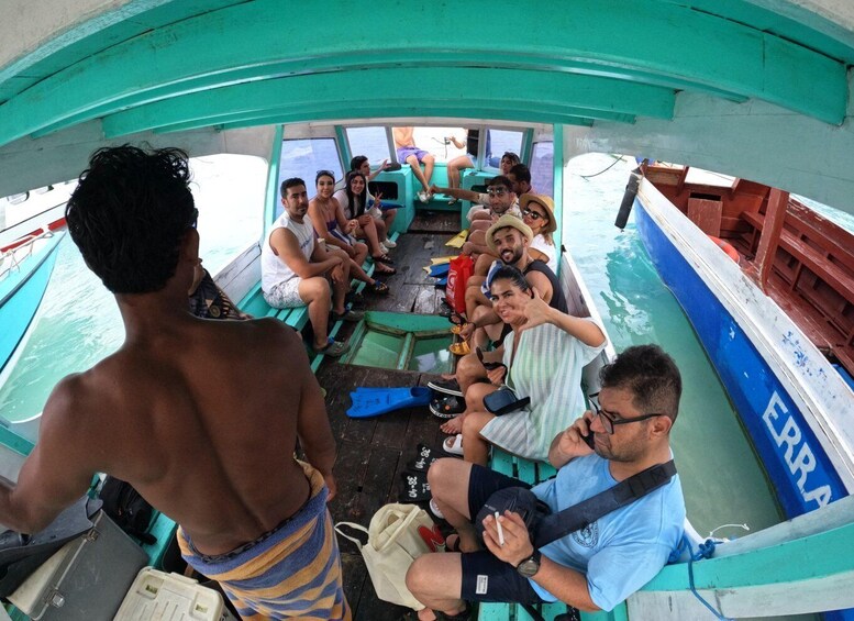 A group of people on a boat with a blue and white hull, some seated and some standing, under a green canopy. 2