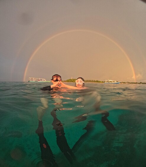 Two people snorkeling in clear water with a rainbow in the background. 3