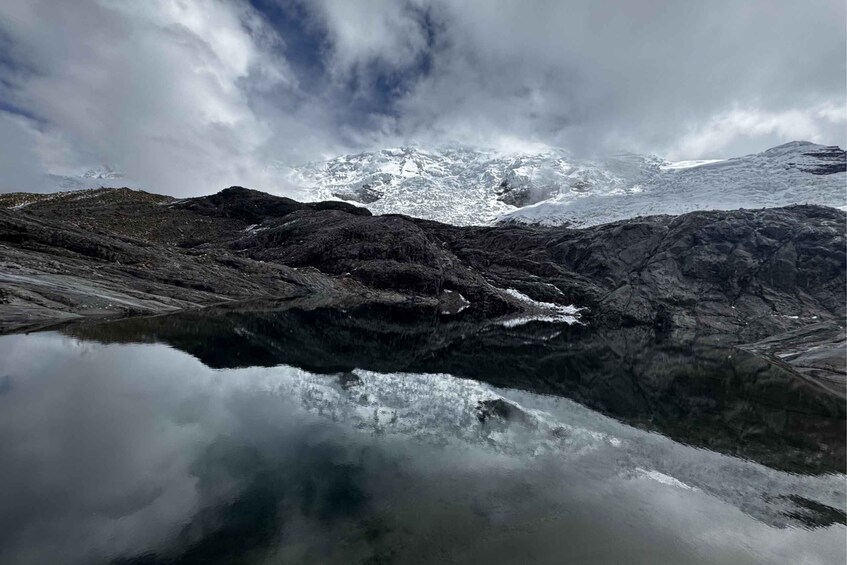 A mountain landscape with a reflective lake, snow-capped peaks, and rocky terrain. 2