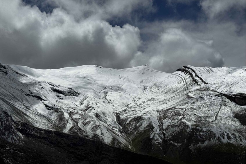 A snow-covered mountain range with rugged terrain and a partly cloudy sky. 5