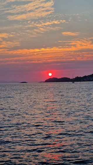 A sunset over a calm sea with a small island in the distance. 2