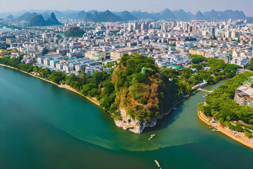 A coastal cityscape with a prominent rocky island, a river, and a dense urban area with buildings. 2