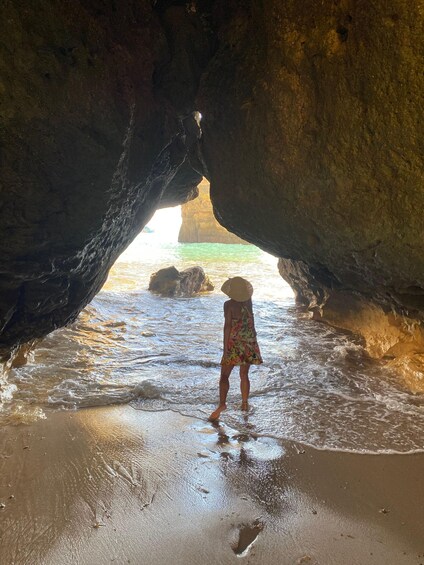 A person standing in a cave entrance with water flowing into it. 3