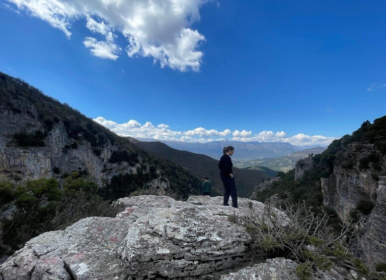 A person standing on a rocky outcrop overlooking a valley with mountains in the distance. 1