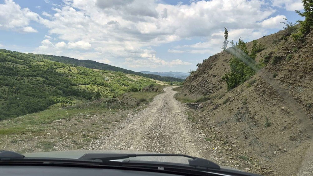 A gravel road winding through a mountainous area with green hills on either side. 4