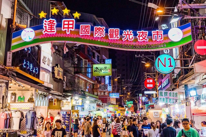 A crowded street market with neon signs and various shops. 4