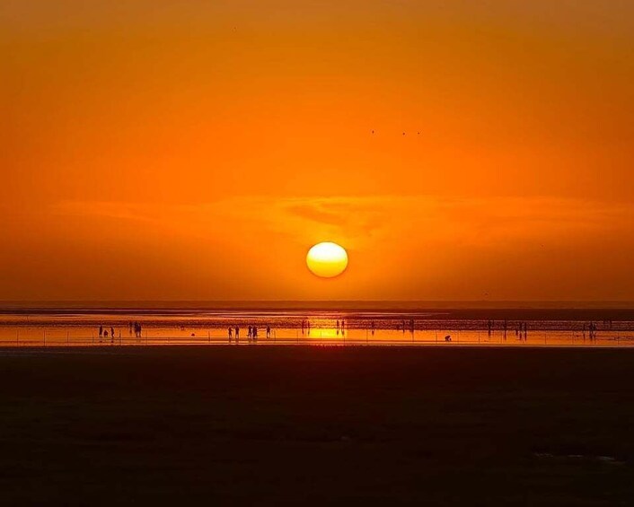 A sunset over a beach with silhouettes of people and a clear sky. 1