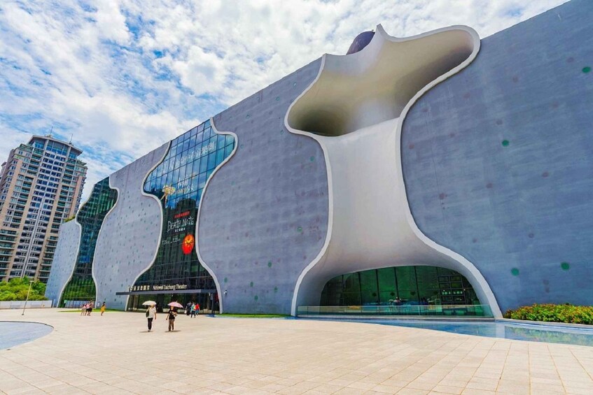 A modern architectural building with a unique wavy design, surrounded by a plaza and other buildings. 3