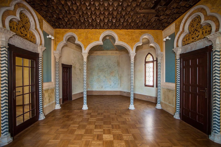 An interior with wooden parquet flooring, white and blue chevron-patterned columns, and ornate arches with intricate designs. 3