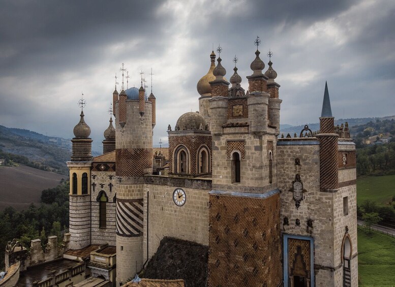A historic castle with multiple towers and a clock tower, surrounded by a rural landscape. 4