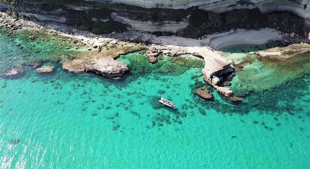 A coastal landscape with clear turquoise waters, rocky formations, and a boat near the shore. 1