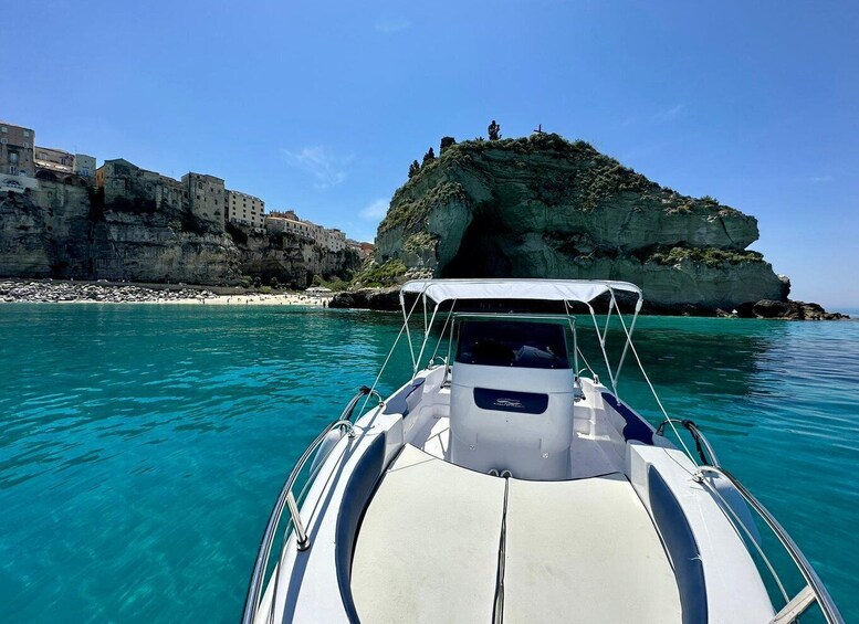 A boat in clear turquoise waters with a rocky coastline and buildings on the shore. 5