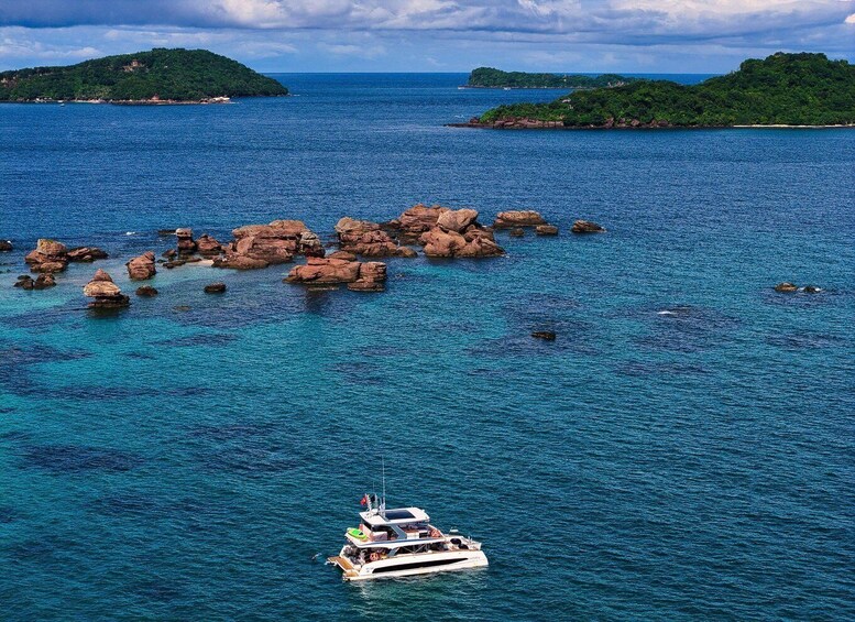 A boat sailing near a cluster of rocks surrounded by clear blue waters and distant green islands. 5